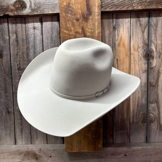 White cowboy hat on a wooden hat rack against a rustic wooden wall.