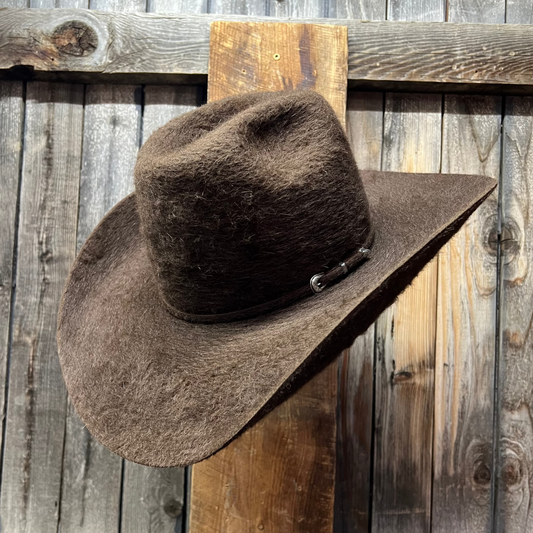 Furry Brown Brown cowboy hat on a wooden stand against a rustic wooden wall