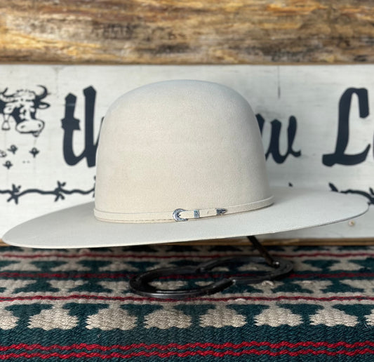 A Furry beige, 10X premium buckskin color felt cowboy hat with an open crown, displayed on a stand against a patterned backdrop.