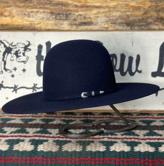 A dark navy blue Rodeo King cowboy hat with a 4 1/2 inch brim displayed on a stand, featuring a silver buckle on the band.