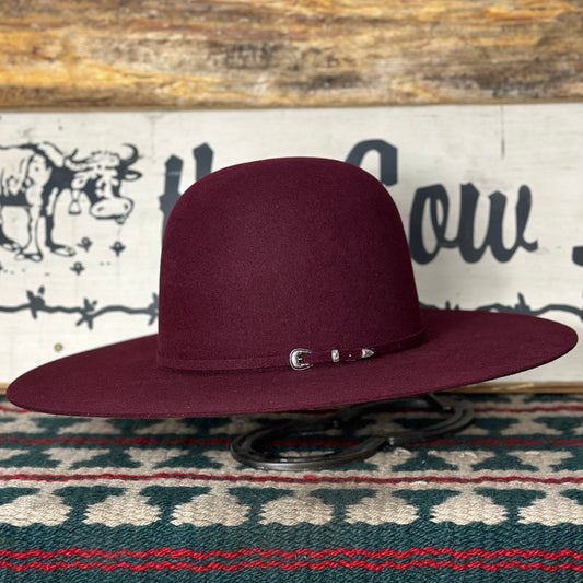 A merlot colored, open crown cowboy hat with a 4 1/2 inch brim, displayed on a stand against a patterned backdrop.