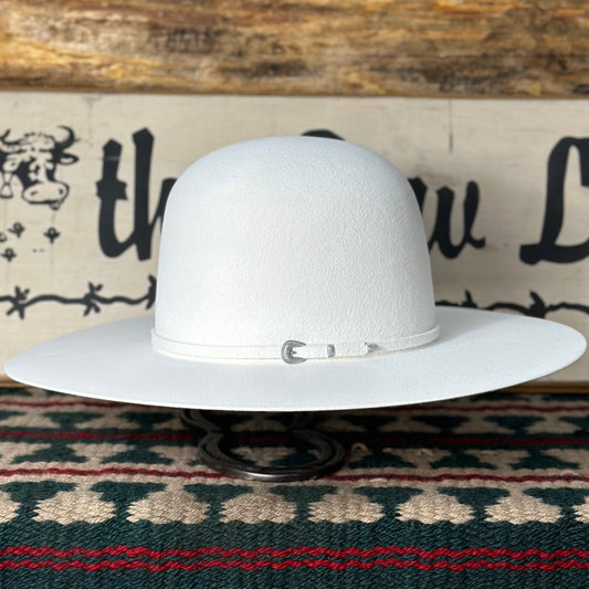White cowboy hat with a 4 1/4 inch brim, hand shaped, with a buckle set on the band, displayed on a stand against a patterned backdrop.