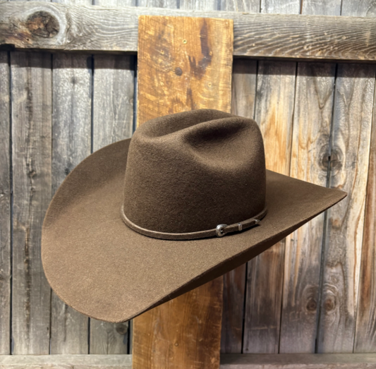 whiskey color cowboy hat with a leather band on a wooden surface against a rustic wooden background