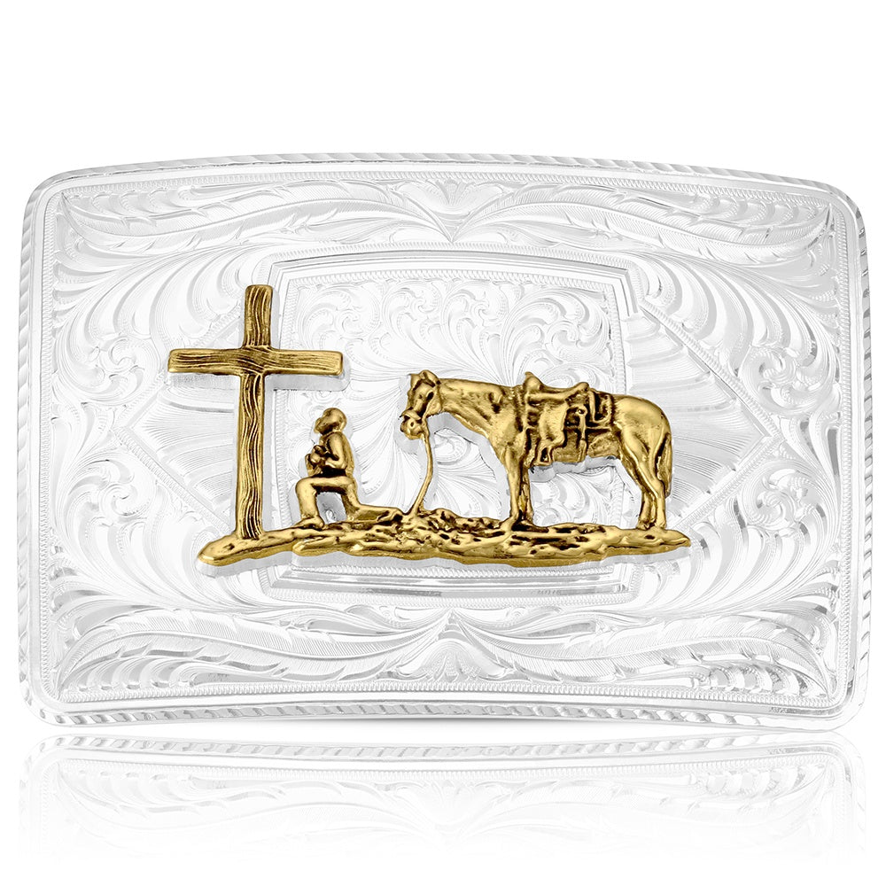 A rectangular clear glass belt buckle featuring a gold-toned relief design of a cross, a kneeling figure, and a horse, all set against an embossed floral pattern.