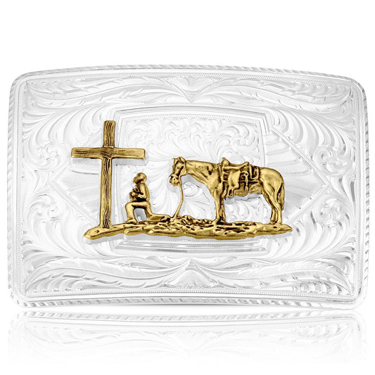 A rectangular clear glass belt buckle featuring a gold-toned relief design of a cross, a kneeling figure, and a horse, all set against an embossed floral pattern.