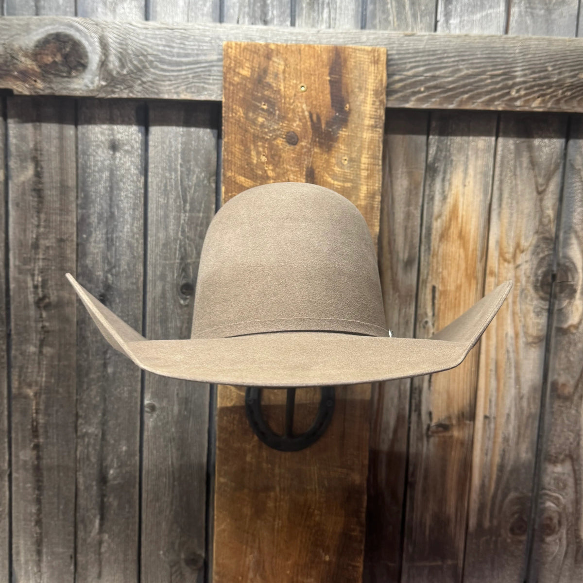 A light brown felt cowboy hat displayed on a rustic wooden wall-mounted stand against a weathered wood plank background.