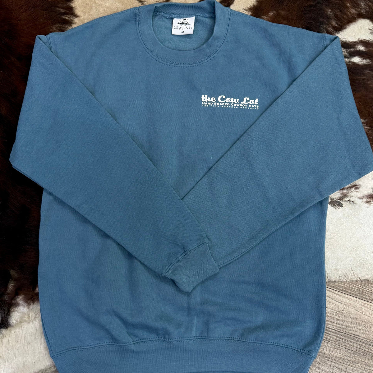 Blue sweatshirt with 'the Cow Lot' logo on a textured surface